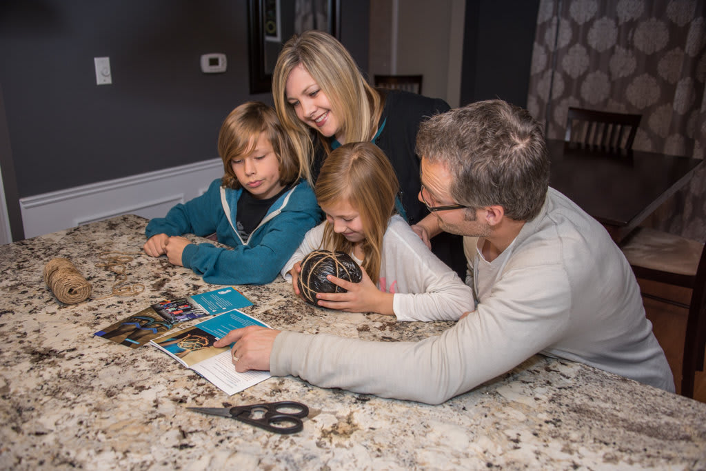 A mom, a dad, a girl and a boy sit together at a table looking at a Compassion magazine. The girl have a handmade ball in her hand.