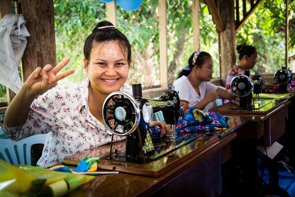 A young woman works at a sewing machine next to two other women.