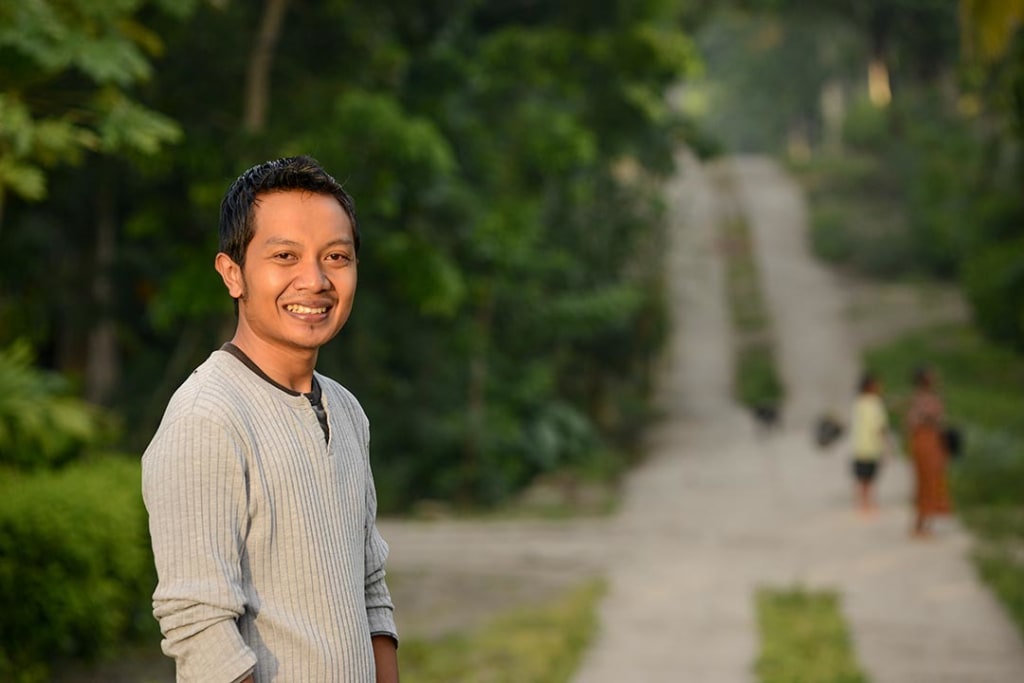 A man stands by a gravel road and smiles