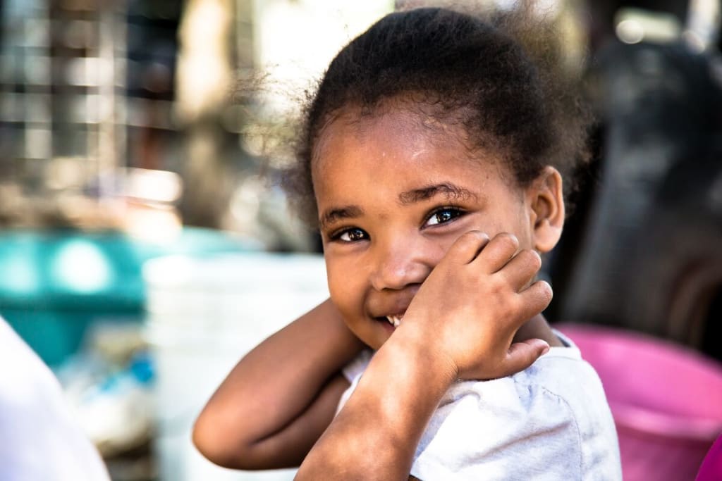 A young girl smiles at the camera with her hands on her face