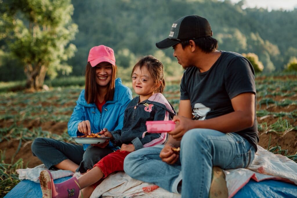 Karunia sits with her mom and dad on a blanket in the hills.