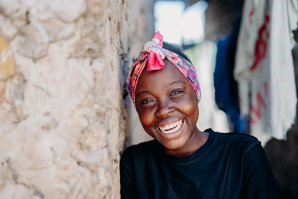 Young woman leans her head against the wall while laughing. She's wearing a pink headscarf and a black shirt.