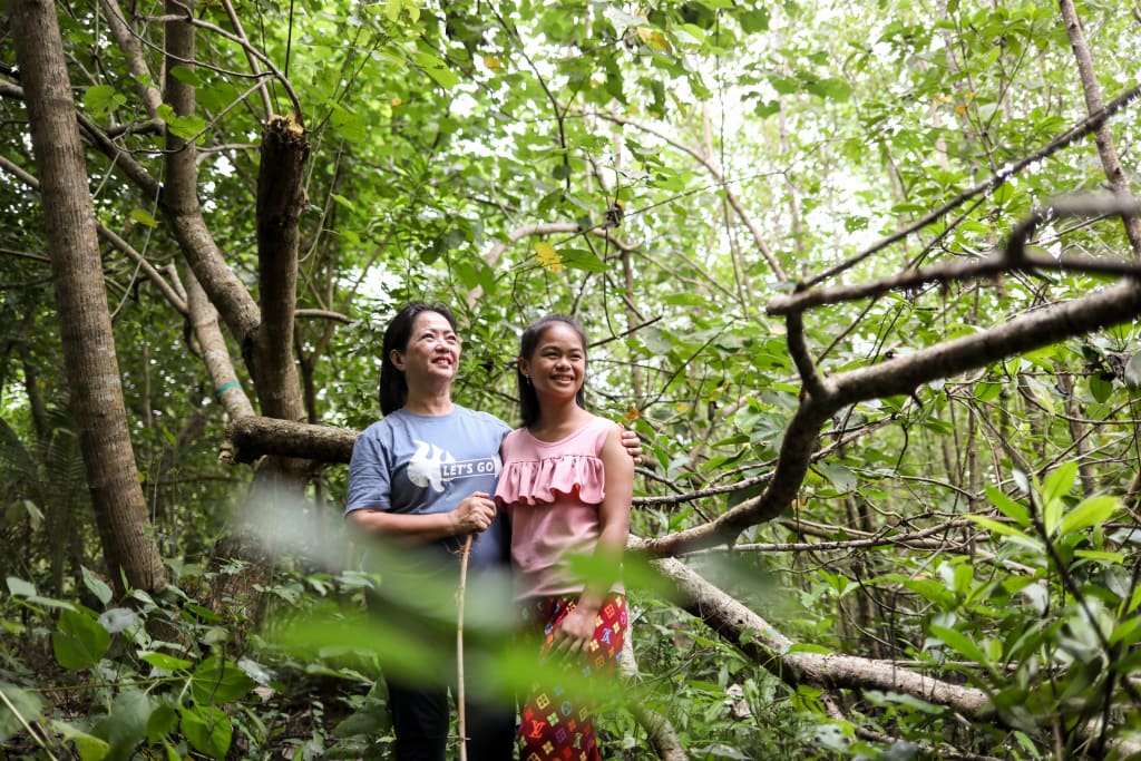 Two women stand in a forest.