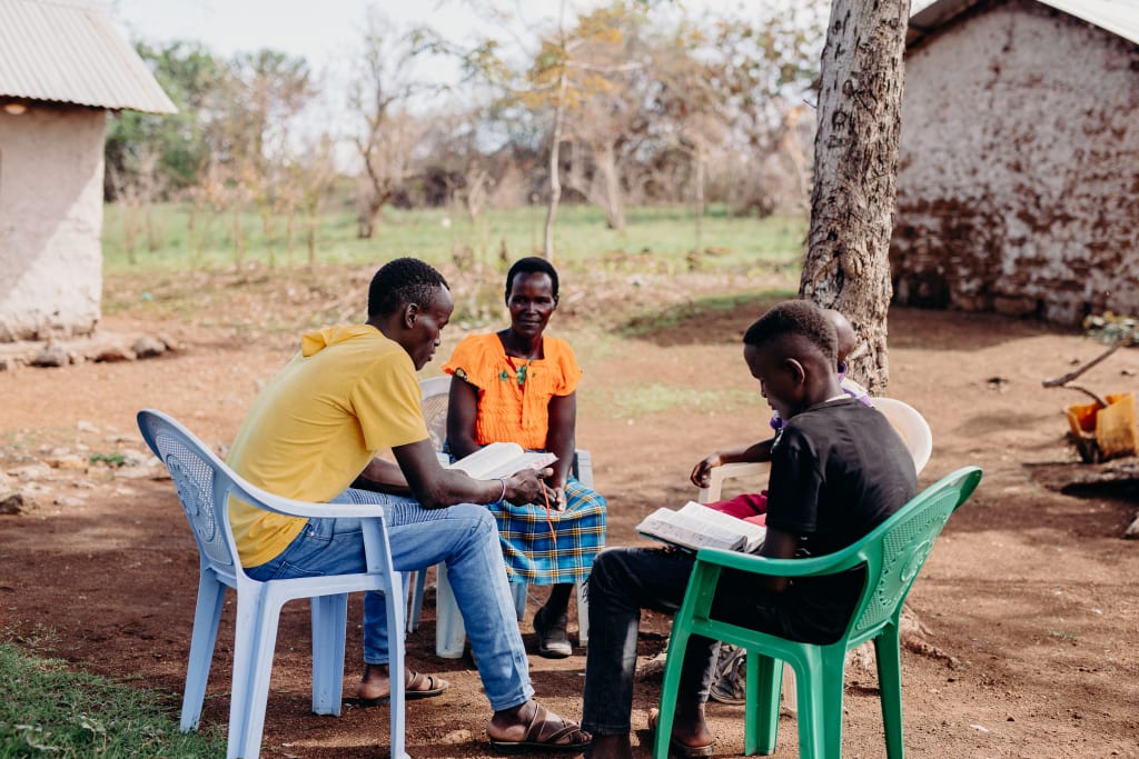 Four people sit in a circle of lawn chairs reading Bibles.