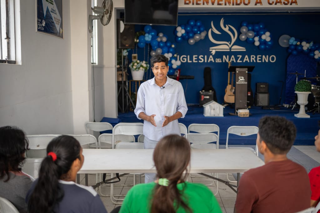 A young man in a blue shirt stands talking to a group of youth.