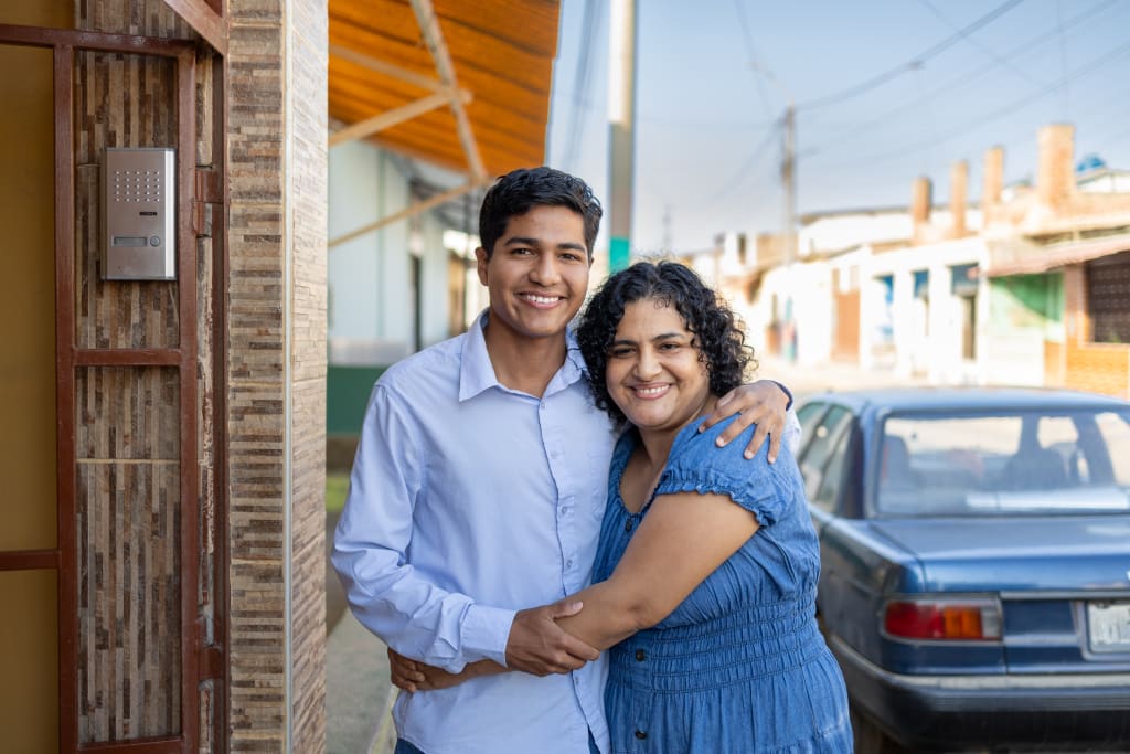A young man in a blue shirt has his arm around his mother who is wearing a blue dress.