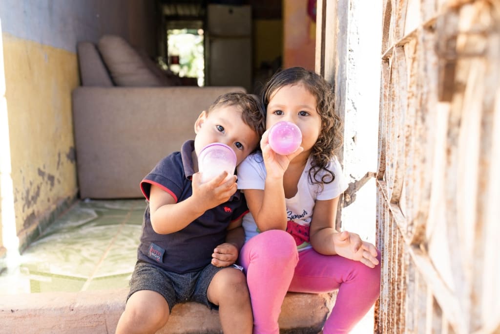 Dávilla and Ithallo are sitting on the doorstep at home drinking milk.