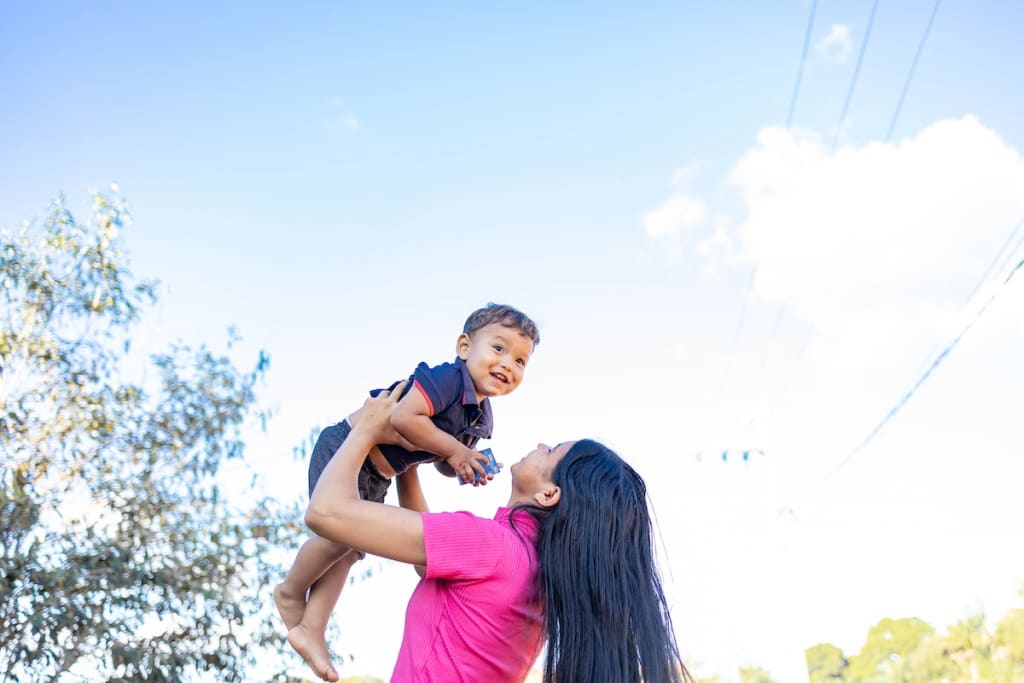 Gabriella is lifting her son, Ithallo, up into the air in front of her house.
