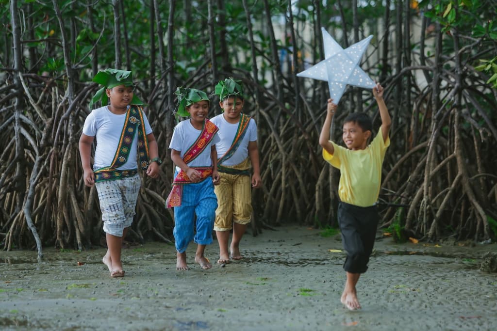 A group of boys dressed as wise men follow behind a boy holding up a cut-out star.