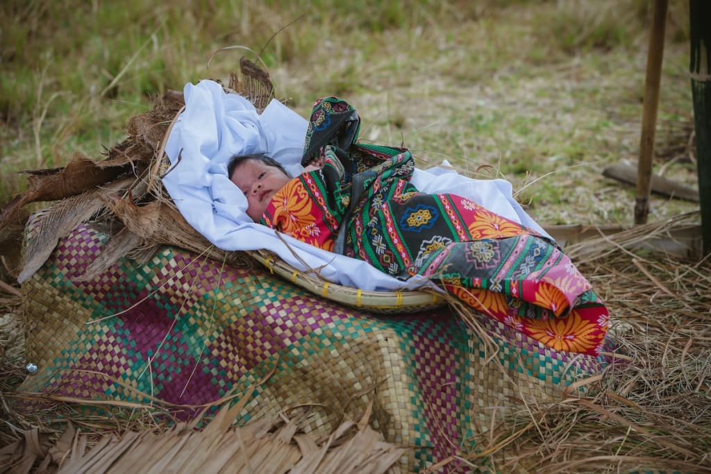A baby wrapped in a colourful shawl lies in a makeshift cradle.