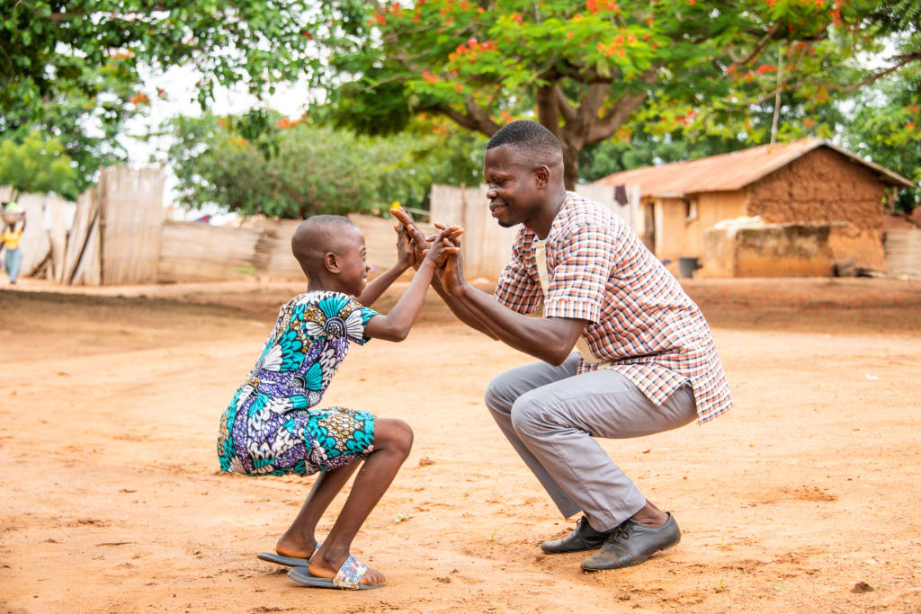 Raphael, a Compassion centre director, plays a game with a young girl in a blue dress.