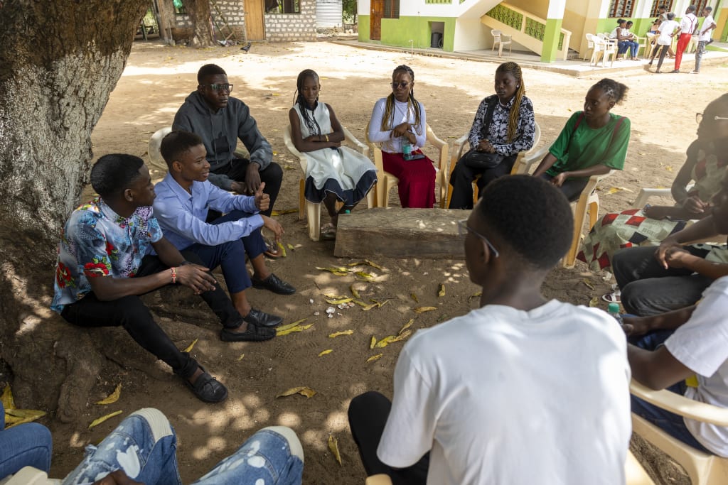A group of youth sit in a circle under a tree.