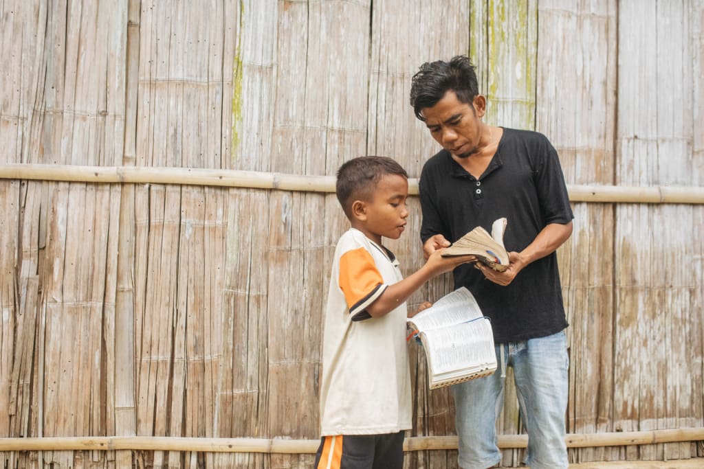 A father and son stand together and look at a Bible.