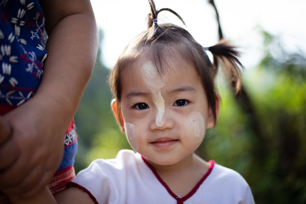 A close up of a young girl in pigtails. She has paste on her face and smiles.