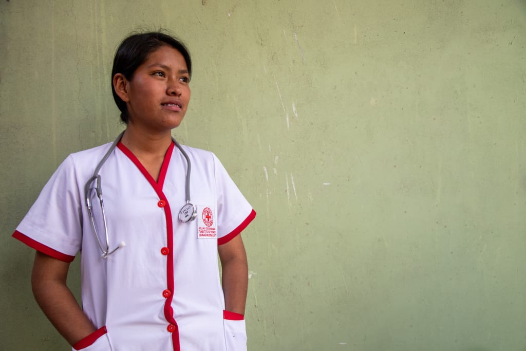 A nurse with a stethoscope around her neck stands against a green wall.