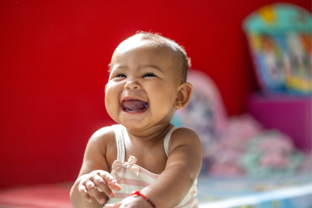 A young baby sits on the floor and laughs.