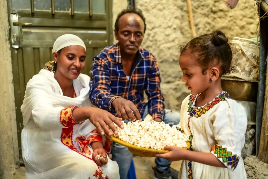 Elbetel is standing with her parents, Anteneh and Tsehaynesh, holding a tray of popcorn for them to share.