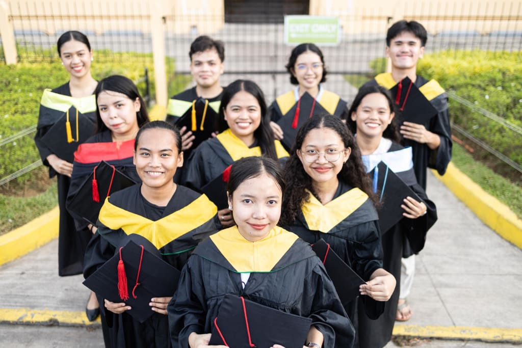 Ten graduates stand together, smiling at the camera. They are each wearing a graduation gown and holding a graduation cap.