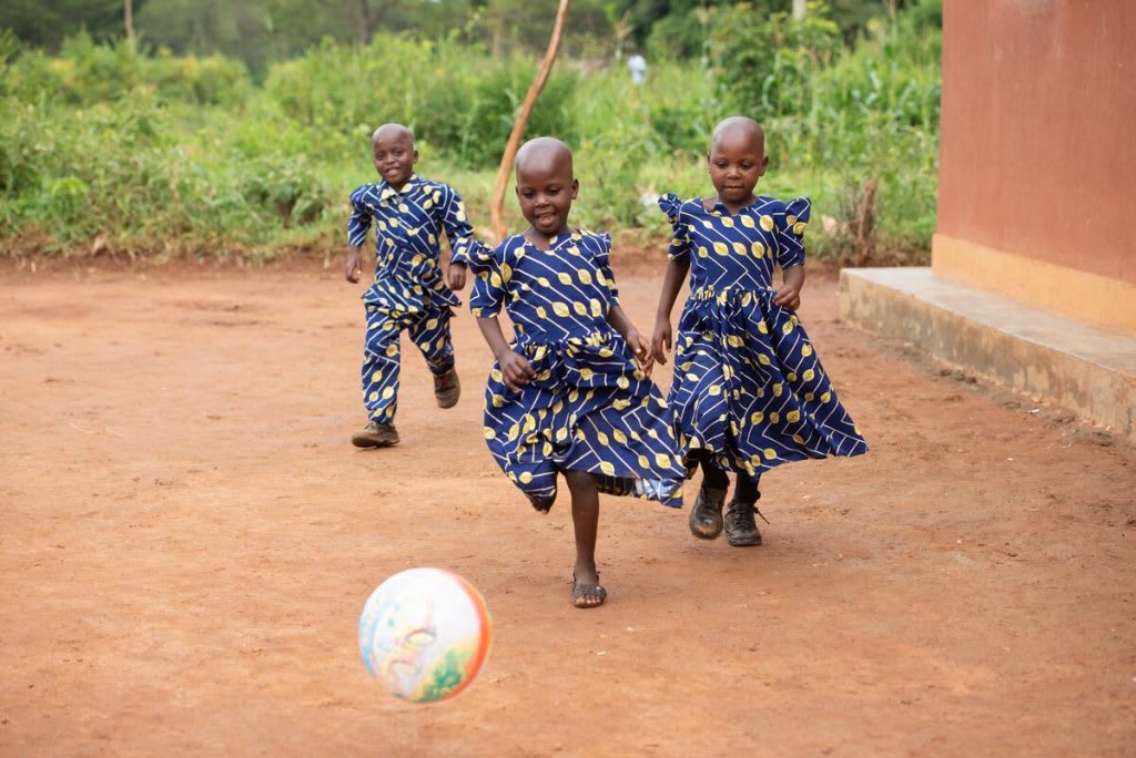 The triplets are wearing matching outfits and chasing a ball.