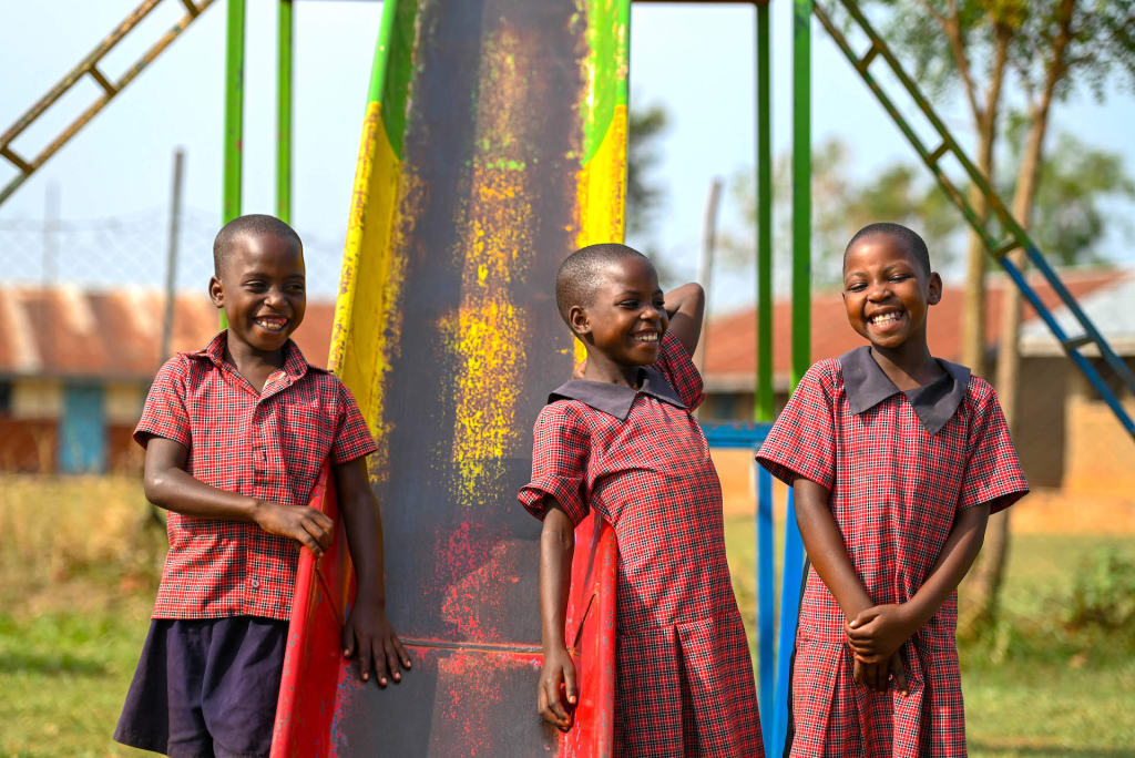Three children wearing red smile against a playground slide. You can see their development from 9 years ago.