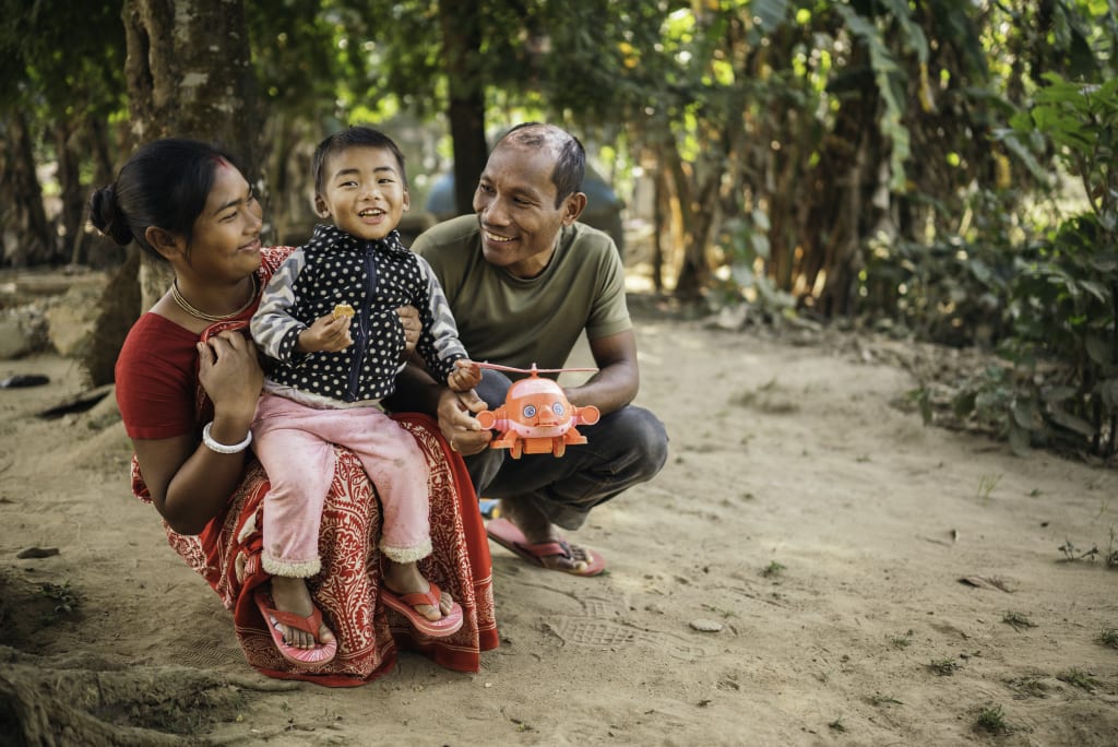 A woman in red and man in green crouch down with a small child between them.