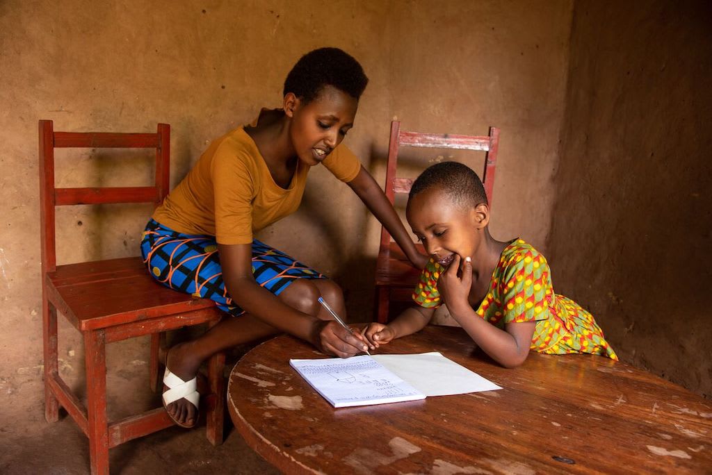 Libradge and Divine sit in their home doing schoolwork.