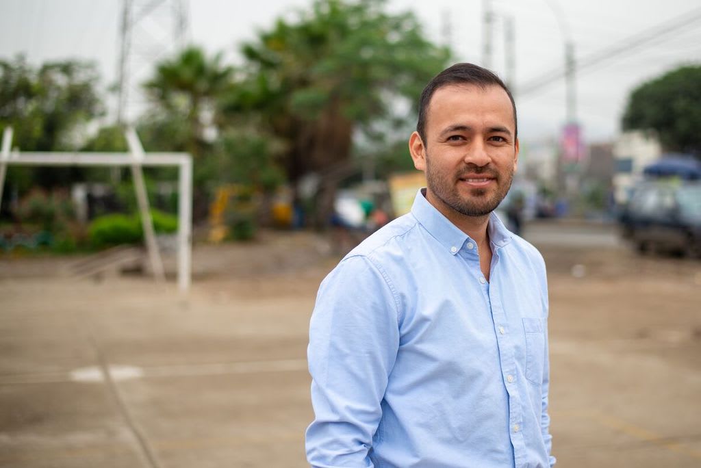 A portrait of John, in a soccer field, dressed in a light blue button-down shirt.