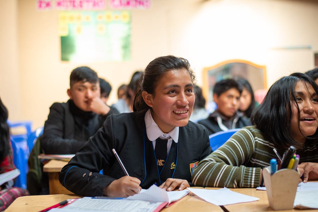 A girl sits at a desk at school, writing in her notebook.