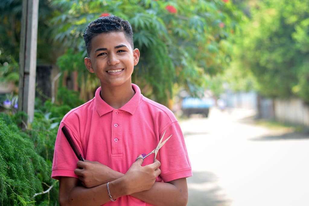 A teenage boy holding scissors and a comb.