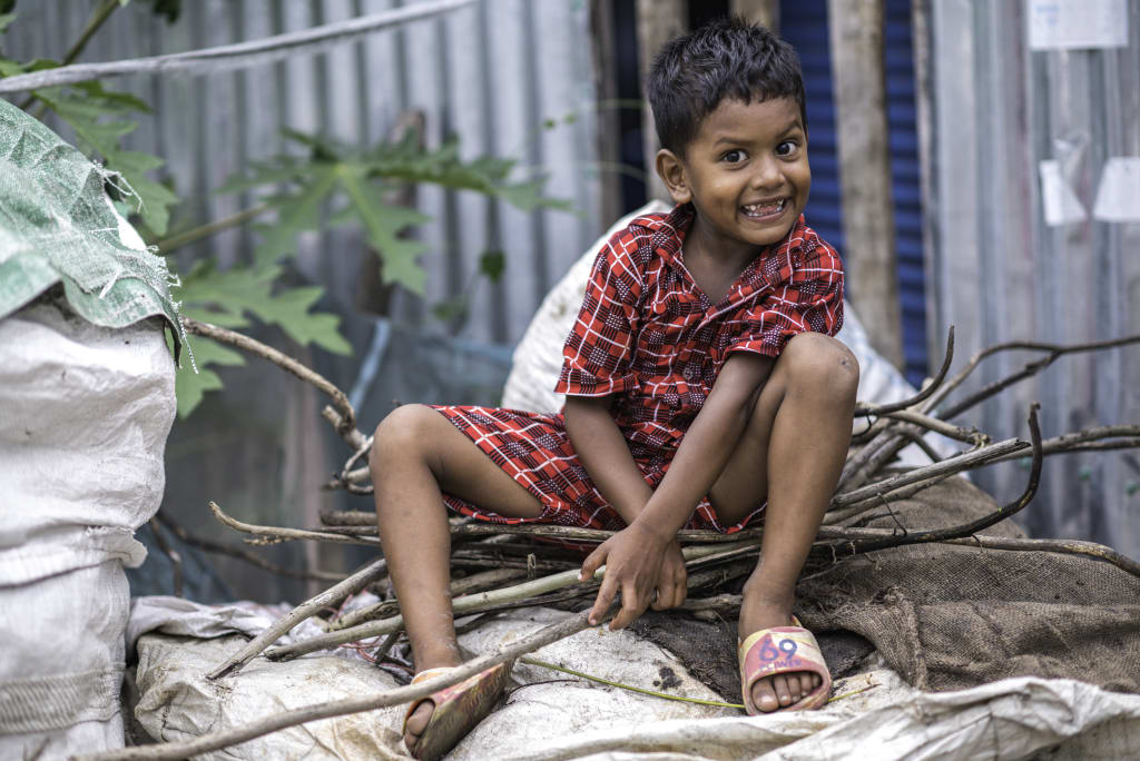 In Bangladesh, 3-year-old Mintu sits on top of the sack that holds the family’s fuel wood (small twigs) that have been collected for cooking.