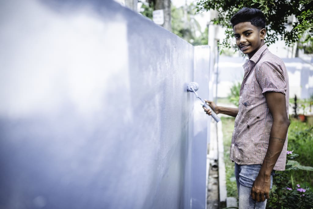 Shanto holds a roller and paints a blue wall.