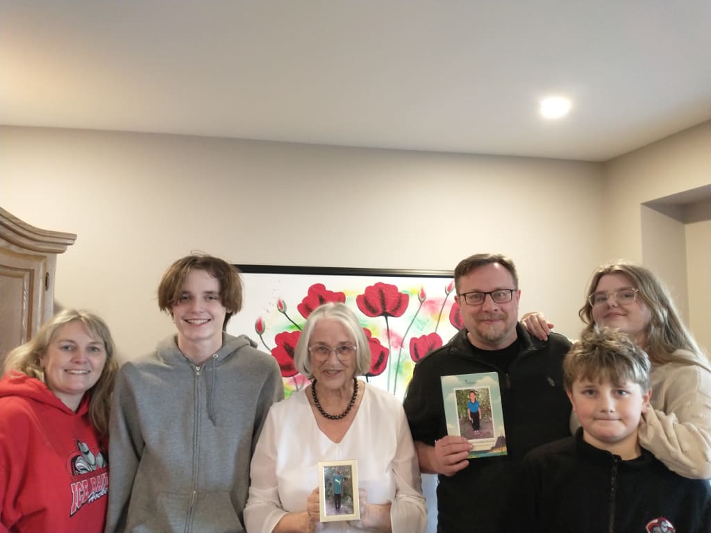 A family stands for a photo and holds two pictures up.