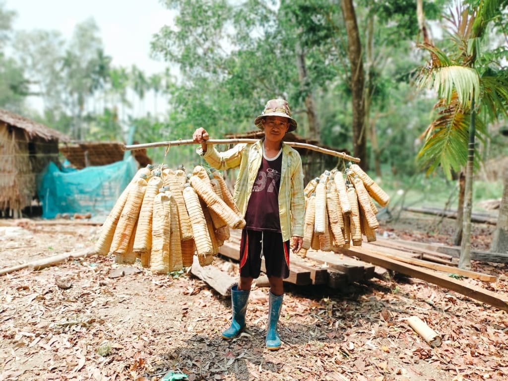 A man holds a pole slung over his shoulder, with tools for catching eels hooked onto the pole.