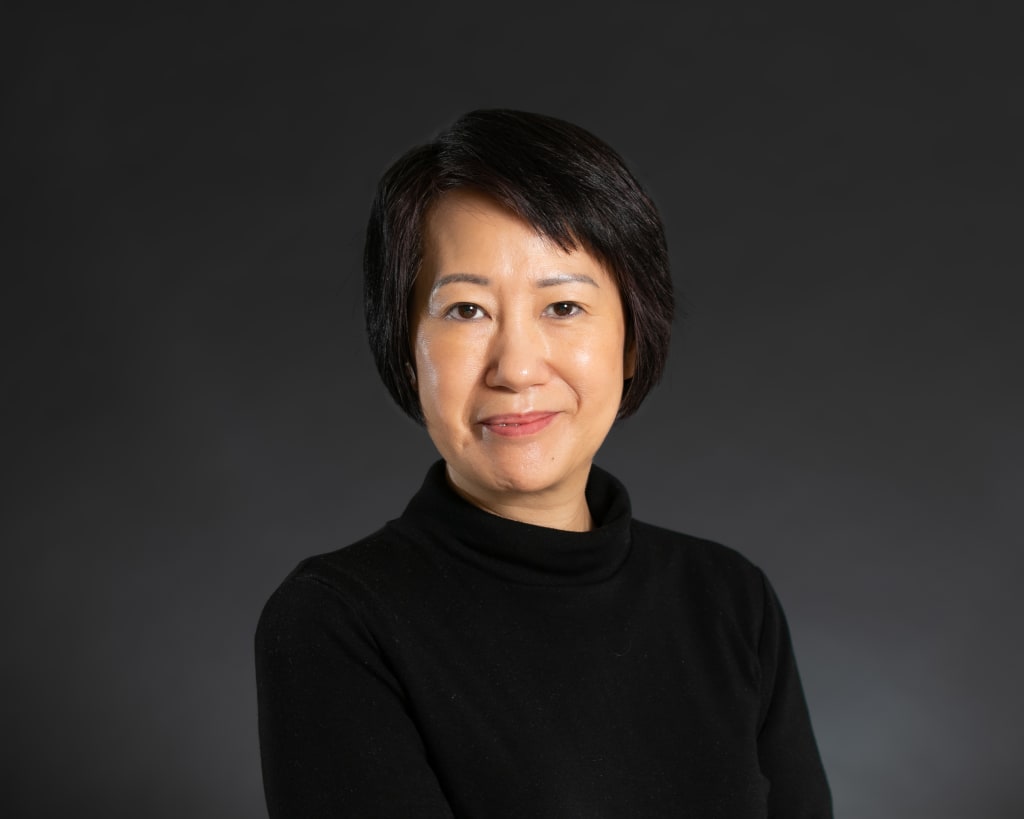 Cudie is standing in front of a grey background, wearing a black sweater and looking straight at the camera.