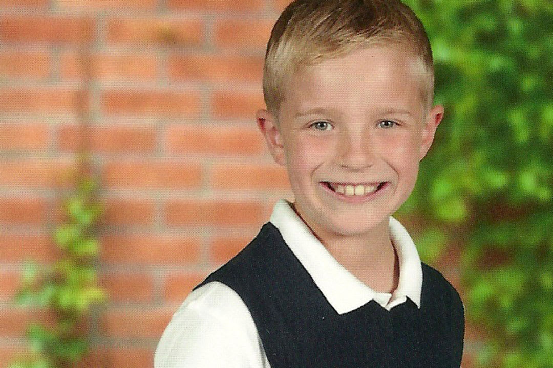 A school portrait of Joshua Riddoch. He's wearing a coloured shirt, a black vest and smiling at the camera