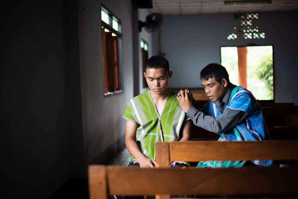 In Thailand, seventeen-year-old Chaiwait and his father Doungdate sit in a dimly lit room and pray together.