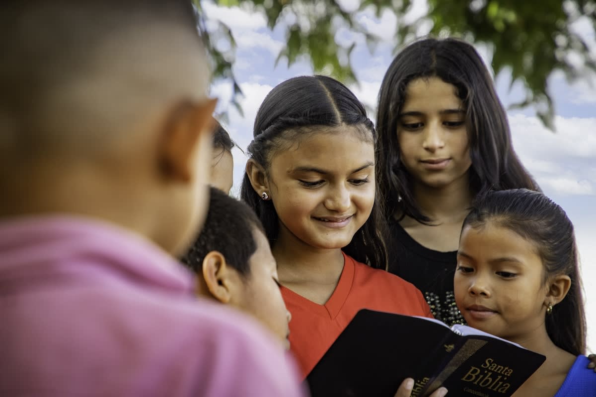 In Honduras, Nicol reads a Bible while holding it up for a group of children around her to see.