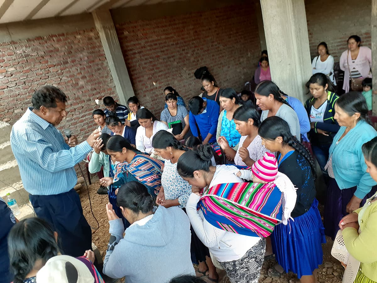 Women gather in the unfinished church building to at church evangelistic meeting. They bow their heads and pray with the pastor.