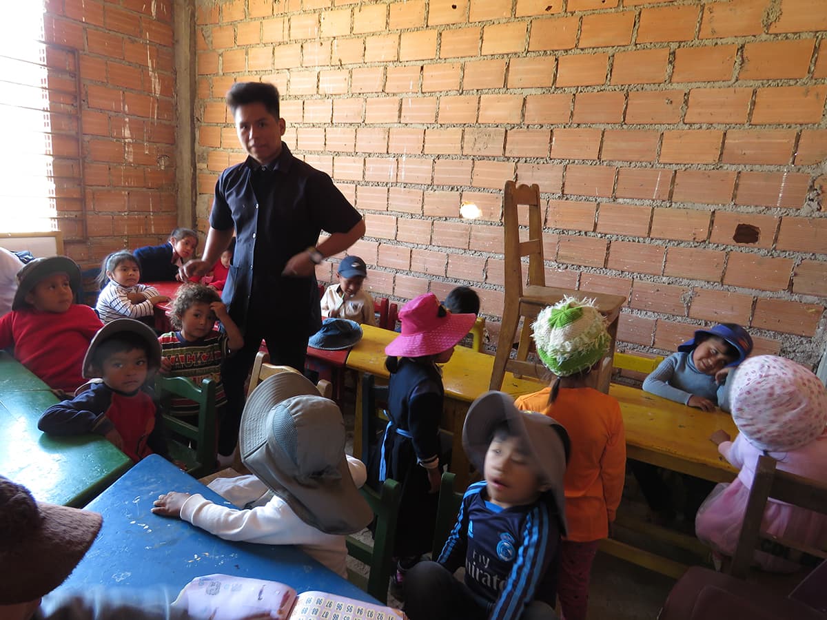 A group of children sit around long tables and listen to leader speak.