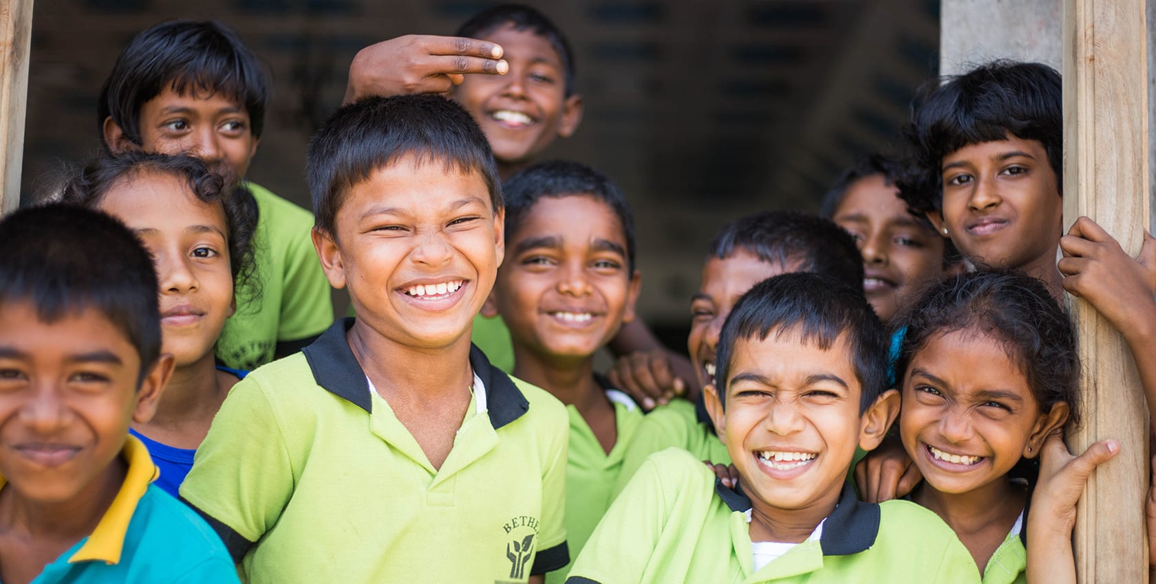 Children stand together wearing green school uniforms