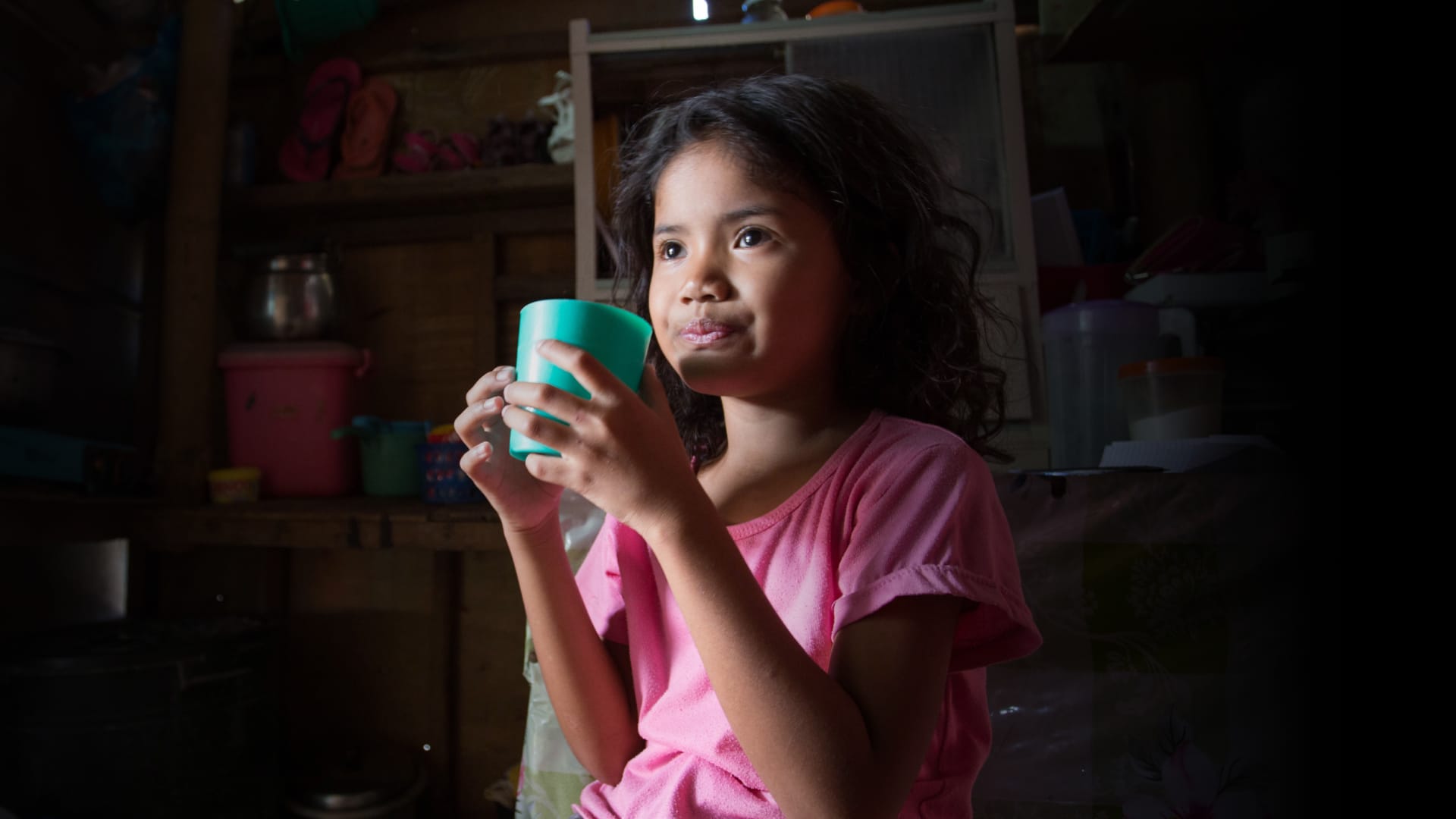 A girl holding a cup and wearing a pink t-shirt