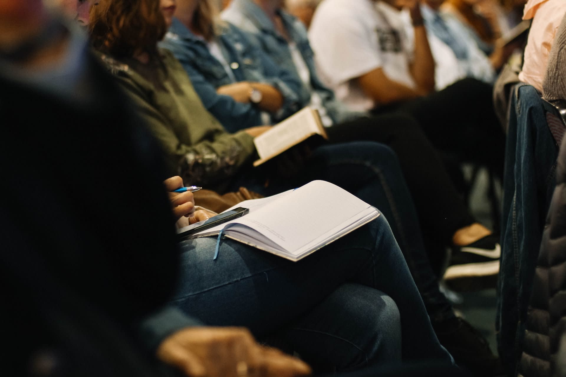 Attendees of a conference or workshop sit in a row with open notebooks on their laps.
