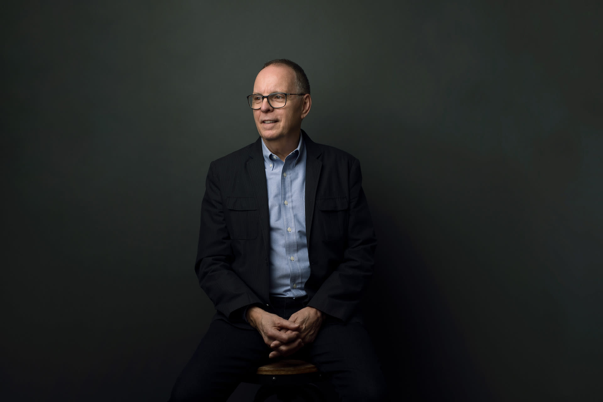 a portrait of Barry. He is wearing a blue shirt and black blazer, sitting and looking into the distance.