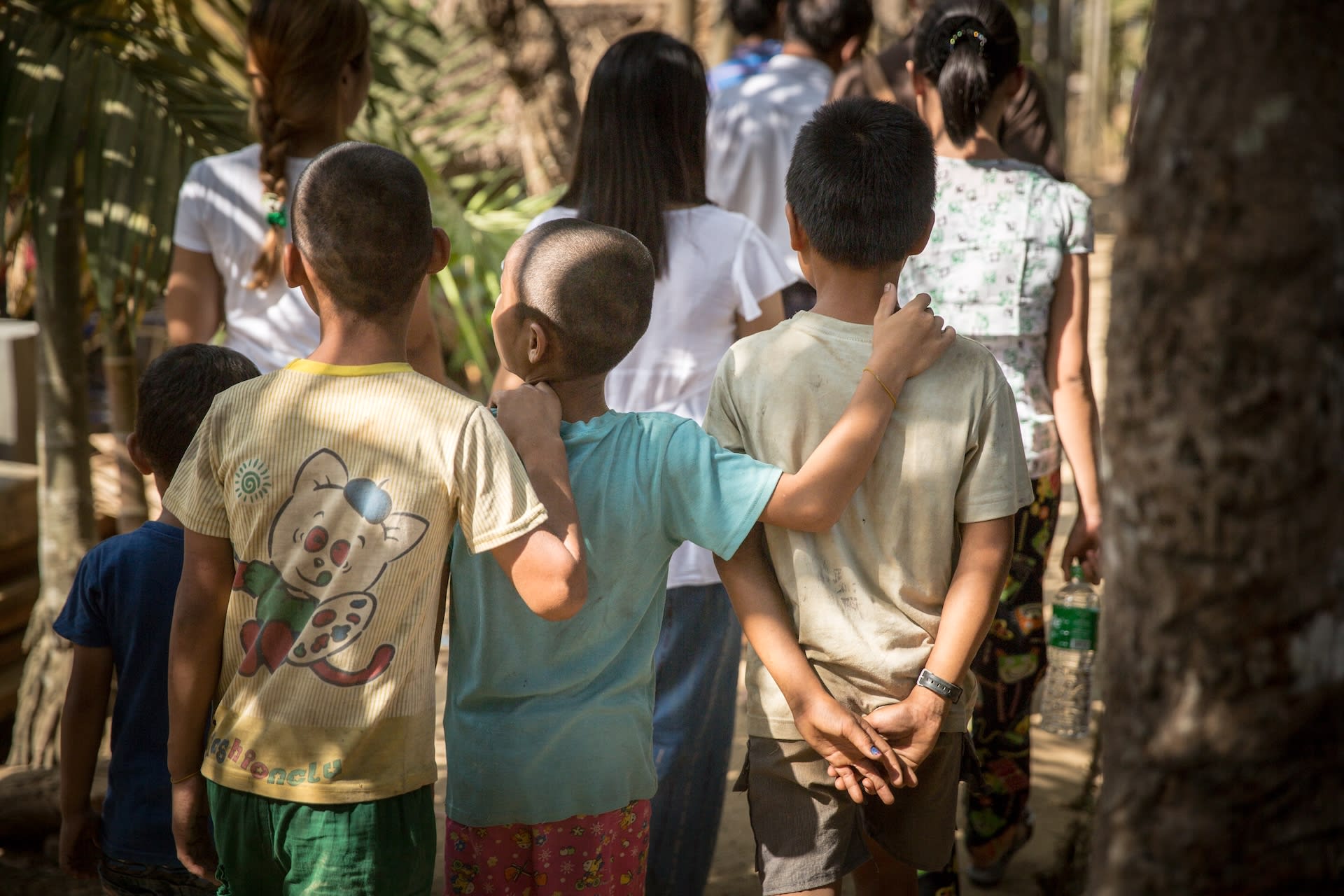 Three young boys with their arms around each other, in a village in Myanmar.