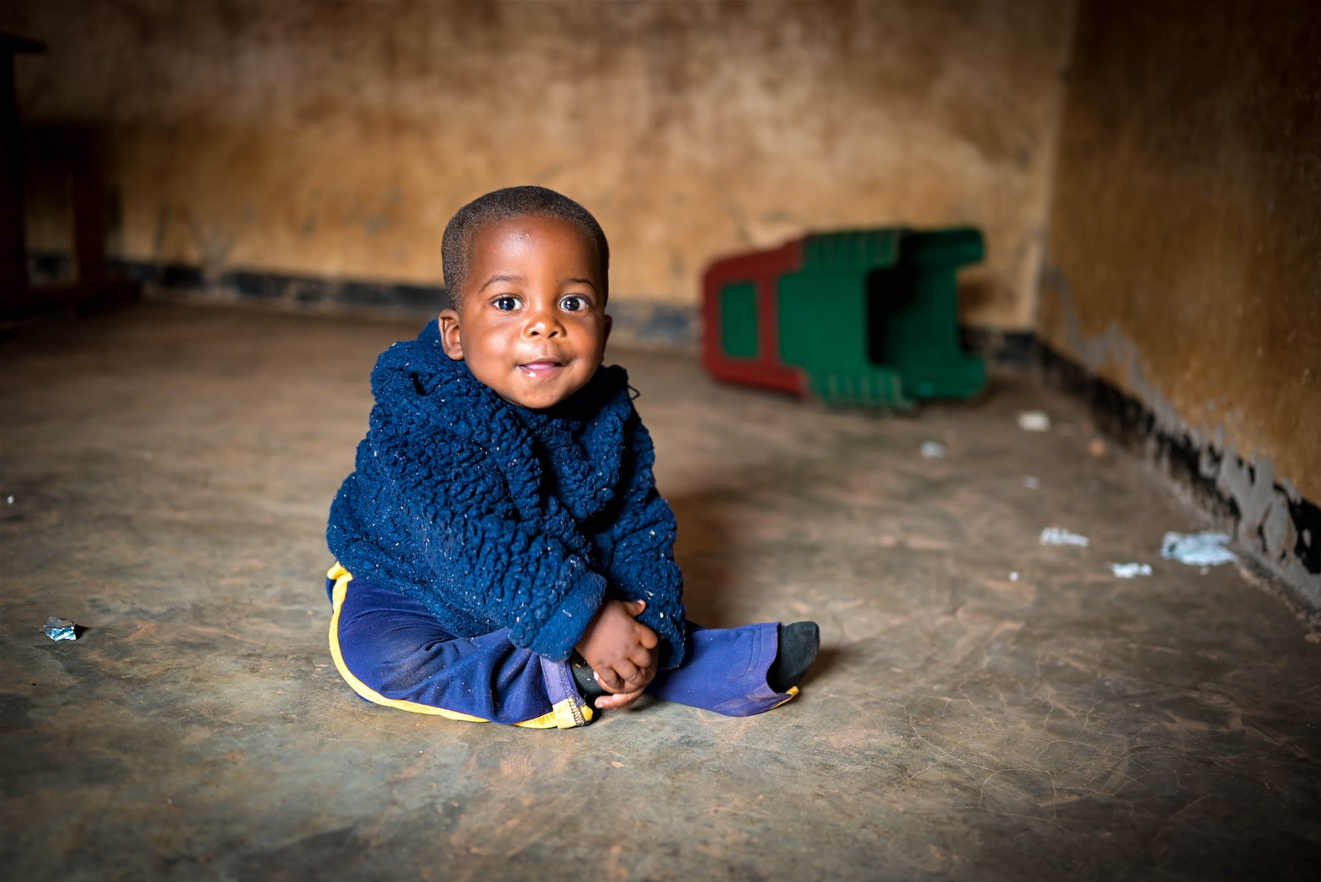 Little baby boy wearing a blue sweatsuit smiles and sits on the ground.