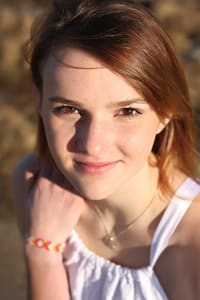 Kaitlin2_LR Kaitlin smiles at the camera in a white top. The sun is hitting her face.
