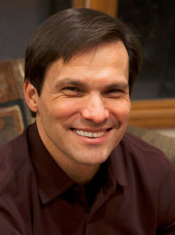 jim-mellado A man in a brown shirt and dark hair smiles at the camera.