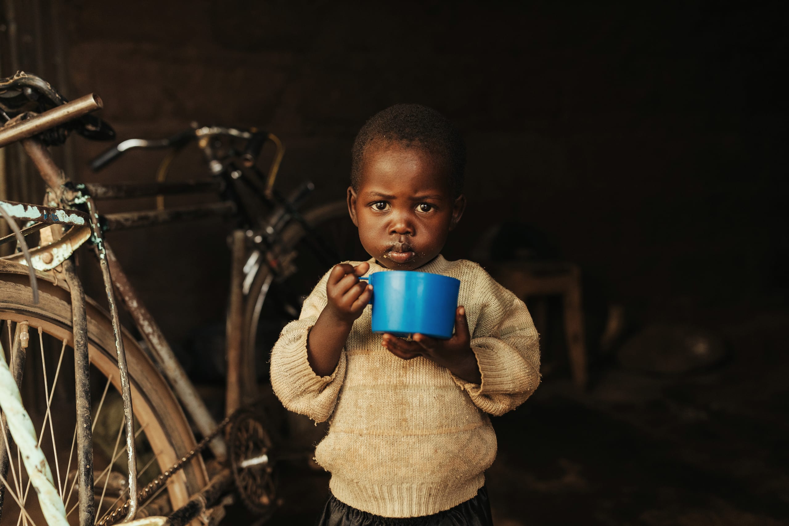 A boy in a cream sweater holds a blue cup