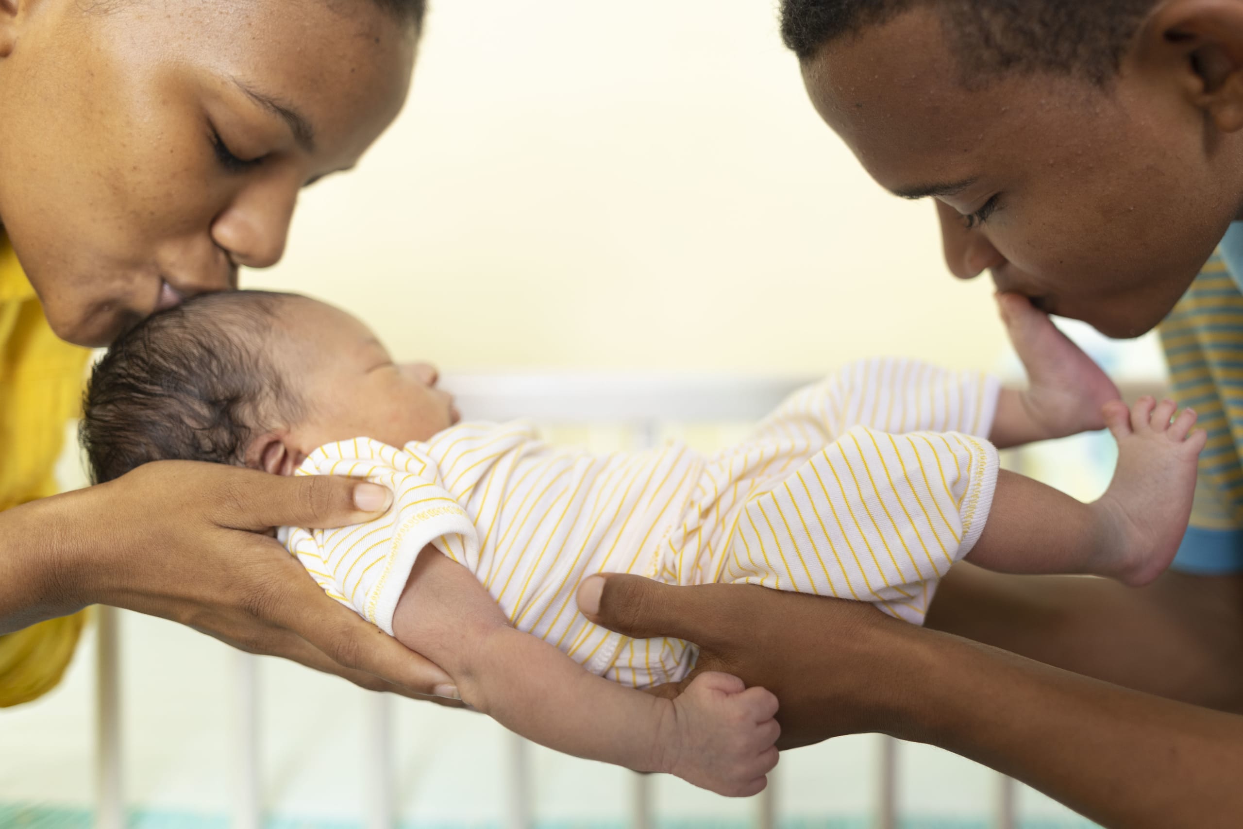 A woman and a man hold a baby between them and kiss the child.