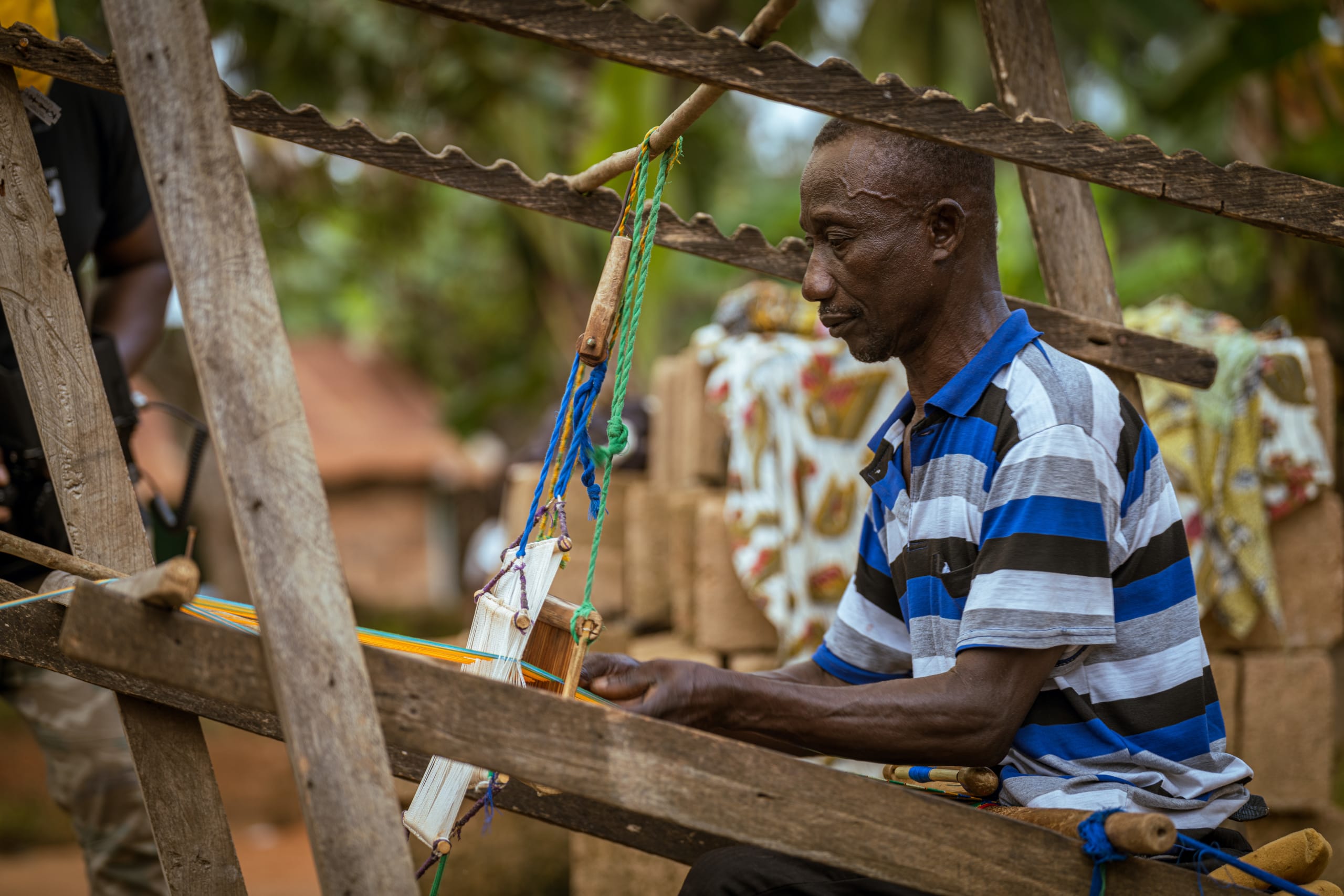 Kwabena, the kente weaver, sits at his loom, weaving a kente stole.